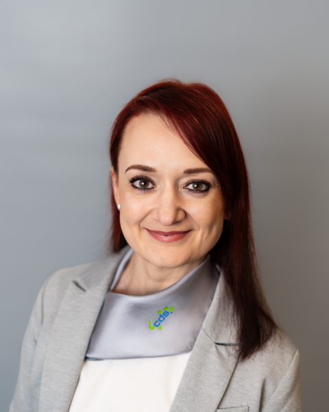 Frau mit rotem Haar, grauem Blazer und cds-Halstuch lächelt in die Kamera.