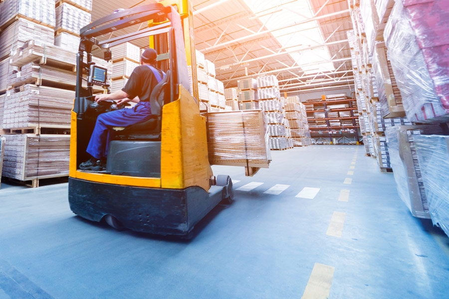 Gabelstapler fährt durch Hochregallager mit gestapelten Paletten.