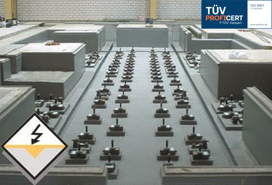 Anlage mit Prüfaufbau, Blitzsymbol unten links, TÜV-Siegel oben rechts.