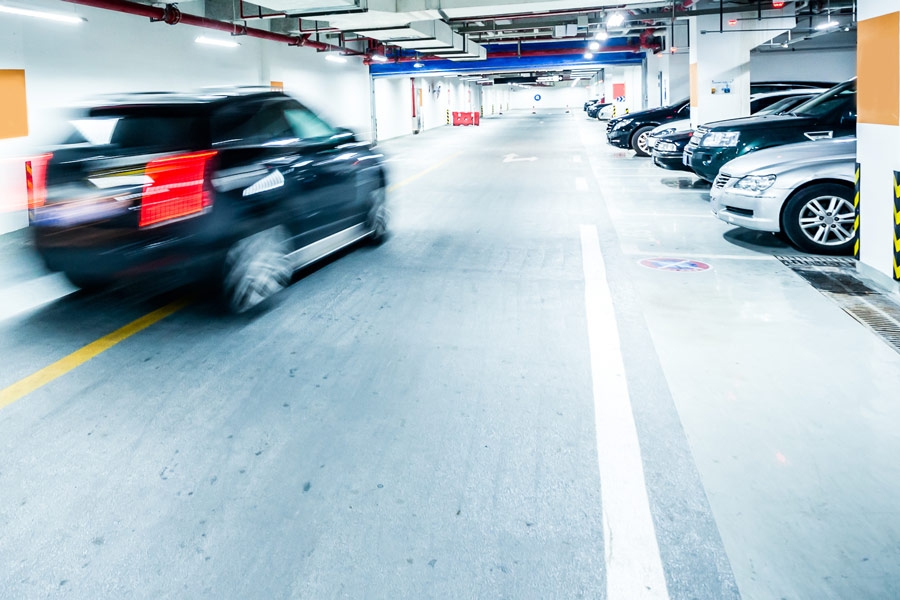Auto fährt durch helle Tiefgarage mit markierten Stellplätzen.