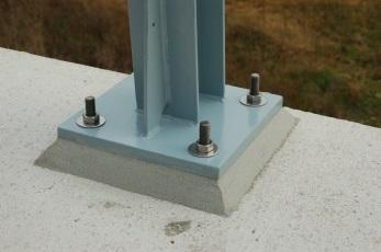 Metallstütze mit vier Schrauben auf betoniertem Sockel befestigt.