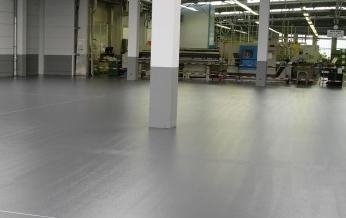 Grauer, ebener Industrieboden in einer großen Produktionshalle.