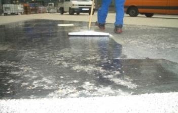 Person verteilt schwarze Beschichtung auf Boden mit Besen.