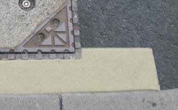 Heller Mörtelanschluss zwischen Asphalt, Randstein und Gussabdeckung.