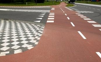 Farbiger Radweg mit weißer Markierung auf einer landstraße.