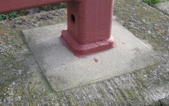 Metallpfosten mit rotem Anstrich auf hellgrauer Bodenfläche.